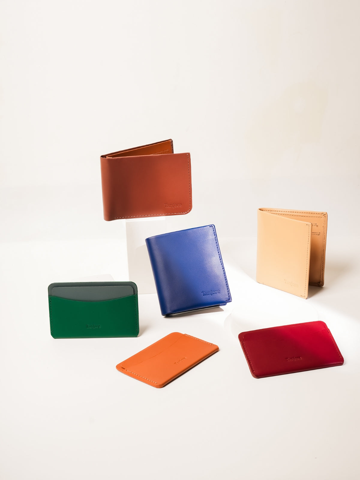 A curated display of the Tanjore collection featuring the Modern Classic 2.0, Reserve Sleeve, and Essential Card Case. These Full Grain Nappa Leather accessories are shown in Tan, Navy, Green, and Plum, highlighting the vibrant color range and Slim Profile.