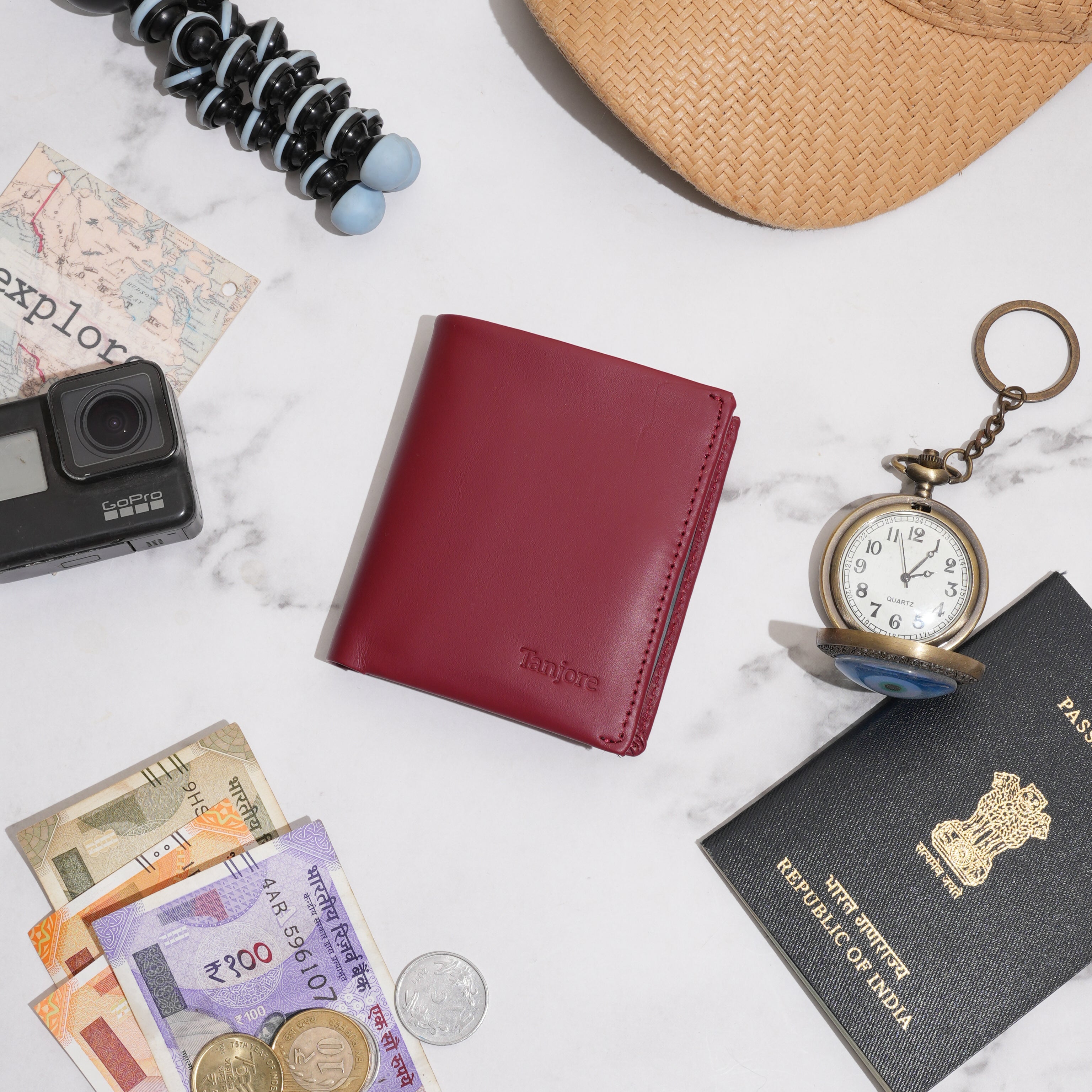 ravel flatlay featuring the Tanjore Reserve Sleeve in Plum alongside a passport, GoPro, and currency. A Slim Profile travel wallet with RFID protection for adventures.