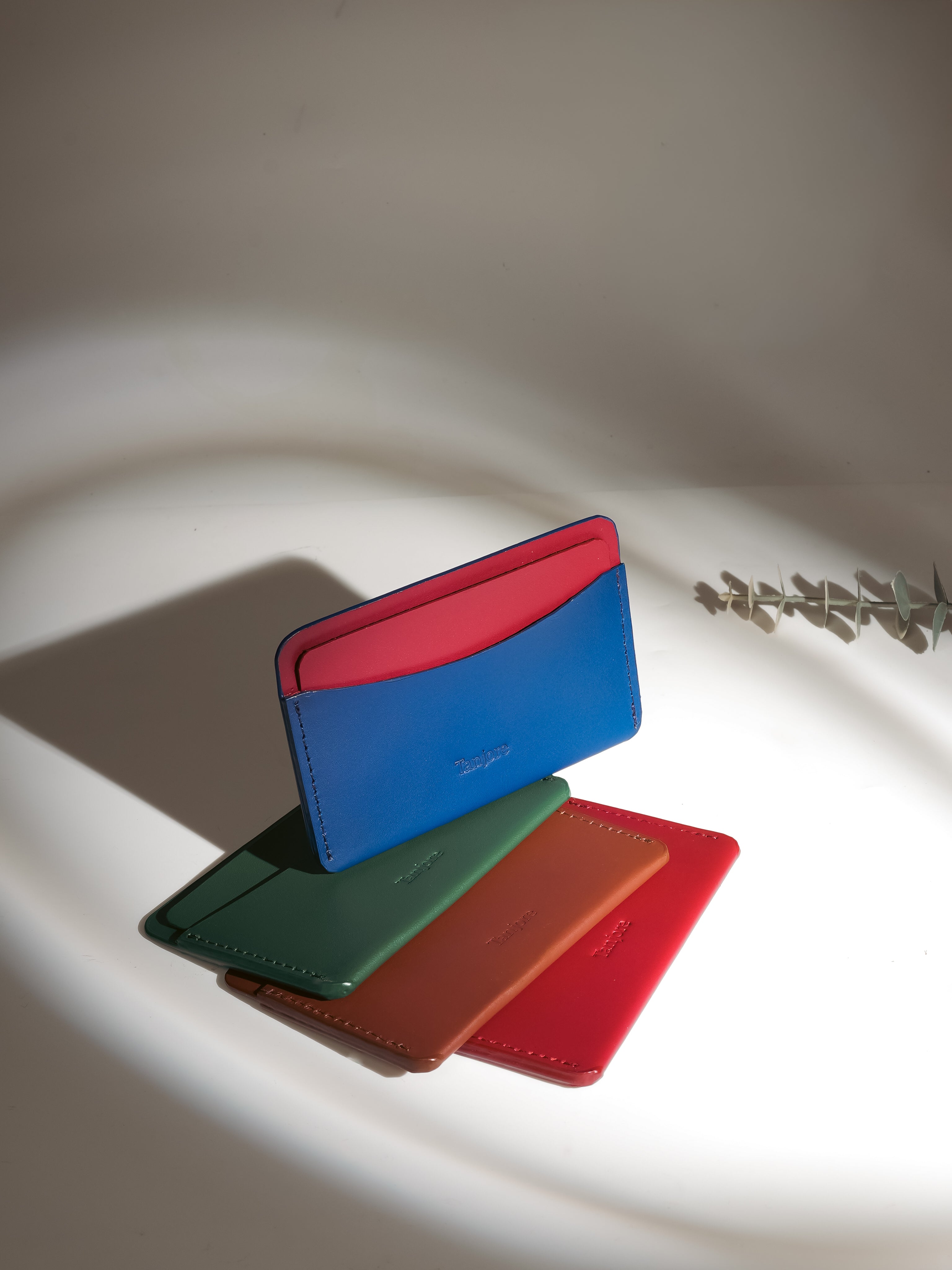 A Navy and Plum leather wallet resting on top of Green, Tan, and Red variations. These Full Grain Nappa Leather cardholders feature a slim profile and come with a 3 year warranty.