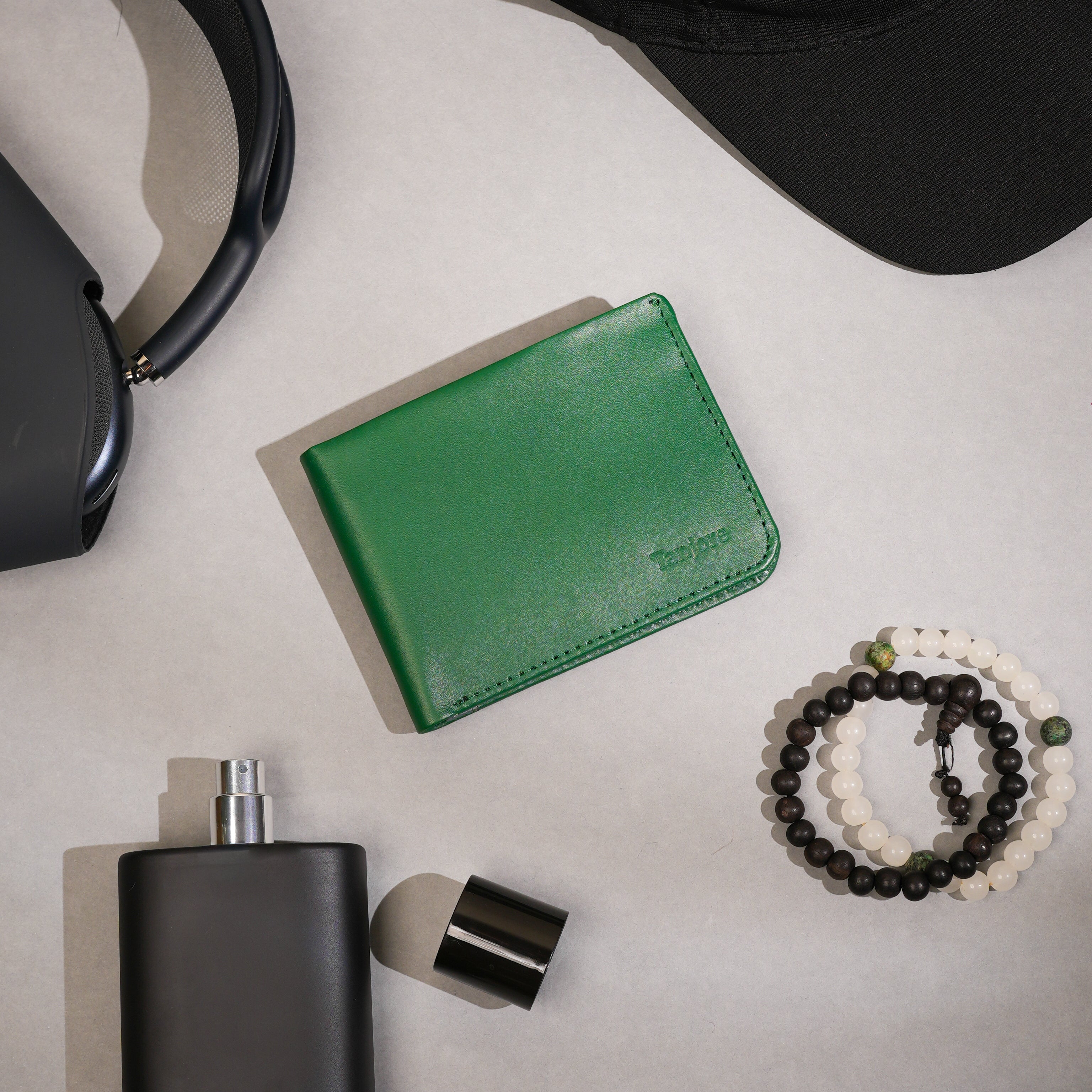 Lifestyle flatlay featuring the Tanjore Modern Classic 2.0 in Green, styled with headphones and daily essentials. A Slim Profile bifold crafted from Full Grain Nappa Leather with RFID protection and a 3 year warranty.